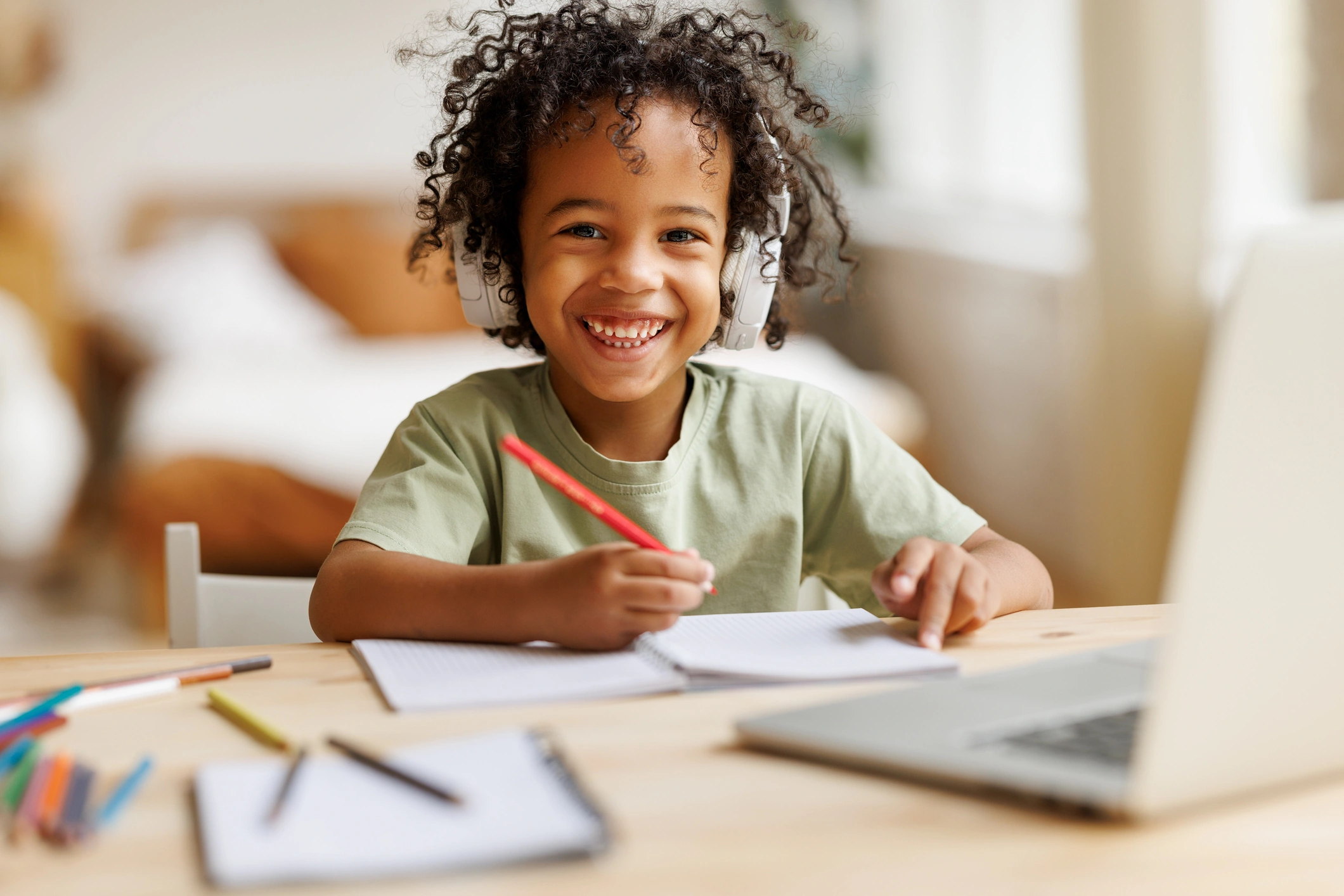 Happy Child with headphones on and writing in front of laptop