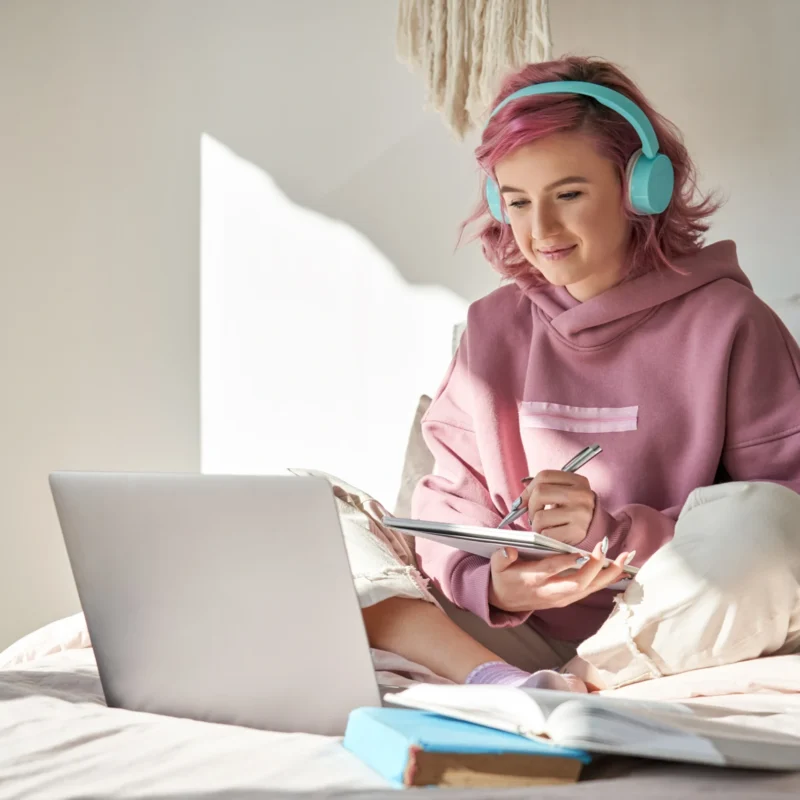 Student engaged in game-based learning for K-12 using a laptop and headphones in a relaxed home setting.